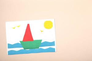 manualidades de papel para niños. aplicación de la creatividad infantil. jardín de infantes y escuela de manualidades. sobre un fondo beige, un barco de papel de colores. foto