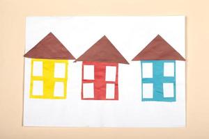 Paper crafts for children. Application of children's creativity. Kindergarten and craft school. On a beige background, multi-colored houses made of colored paper.