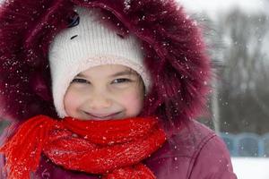 niño en invierno. una niña pequeña con un gorro y una capucha mira a la cámara y sonríe. foto