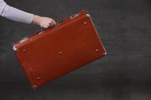 In hand is a brown retro suitcase on a gray background. photo