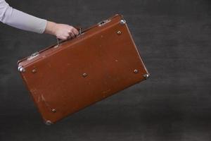 In hand is a brown retro suitcase on a gray background. photo