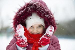 Child in winter. A little girl in a warm hat and hood looks at the camera and smiles. photo