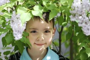 bielorrusia, ciudad de gomil, 16 de mayo de 2016. calle de la ciudad. un hermoso niño está parado junto a un arbusto de lilas y sonríe. foto