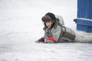 A little boy in a fur hat lies on the snow. Child in winter. photo