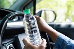 la conductora asiática sostiene agua fría para beber en el automóvil, es peligrosa y corre el riesgo de sufrir un accidente.