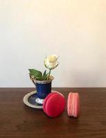 flor de rosa blanca en una taza elegante y dos macarons en una mesa de madera, espacio para texto, vista vertical foto