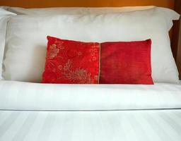 Close up A red Chinese style fabric scatter cushion, backrest pillow, placed in front of double white pillows on the hotel bed, turn down service with copy space photo