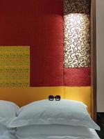 gafas de sol sobre almohadas blancas dobles en la cama, con tela de cabecero de diseño en colores rojo y amarillo, decoración, interior, hotel, bangkok foto