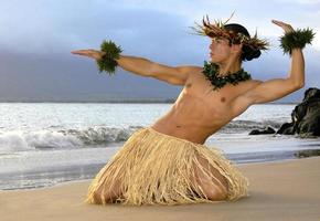 este bailarín de hula masculino muy guapo se presenta en una posición tradicional en la arena justo en la arena mojada al lado del océano. foto