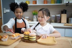 dos niños pequeños felices cocinando juntos, sacando masa, parados en una encimera de madera en una cocina moderna, lindos caseros foto