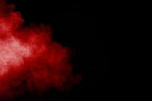 Red powder explosion cloud on black background. Freeze motion of red color dust  particles splashing. photo