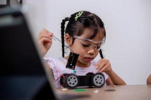 los estudiantes asiáticos aprenden en casa codificando automóviles robot y cables de placas electrónicas en tallo, vapor, ingeniería matemática, ciencia, tecnología, código informático en robótica para conceptos infantiles. foto