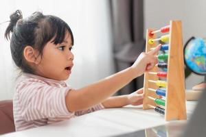 A young cute Asian girl is using the abacus with colored beads to learn how to count at home photo