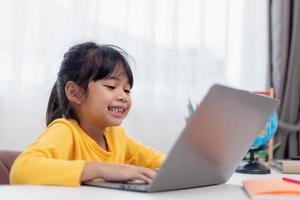 First day at school. Asian little girl using a laptop computer, studying through online e-learning system. photo