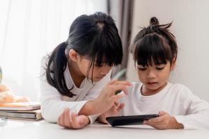 Concept kids and gadgets. Two little girls siblings sisters look at the phone and smile. They hold a smartphone watch videos, learn, play games, speak online. Internet for children. Parental control photo