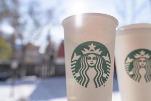 Marinette,WI,USA - Nov14, 2023- Cups of Starbucks Hot Coffee put on white snow in winter garden, fresh and hot beverage take away concept.Starbucks Cafe Coffee Shop. photo