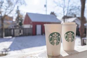 Marinette,WI,USA - Nov14, 2023- Cups of Starbucks Hot Coffee put on white snow in winter garden, fresh and hot beverage take away concept.Starbucks Cafe Coffee Shop. photo