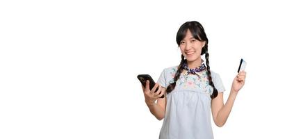 Portrait of beautiful happy young asian woman in denim dress holding credit card and smartphone on white background. studio shot photo