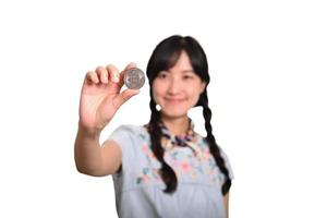 Portrait of beautiful happy young asian woman in denim dress holding crypto currency coin on white background. photo