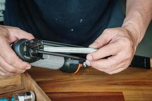 carpenter using nail gun or brad nailer tool ,load a top loading stapler  in a workshop ,furniture restoration woodworking concept. selective focus photo