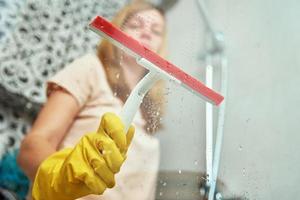 Woman cleaning bathroom cabine with scraper photo