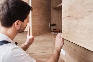 Man open kitchen cupboard. Repairman in uniform fixing cabinet at kitchen photo