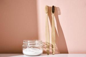 Two bamboo toothbrushes and tooth powder on pink background photo