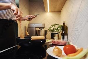 mujer cocinando salsa boloñesa y usando smartphone foto