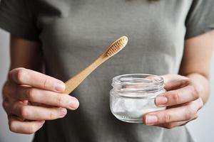 Woman holds bamboo toothbrush and soda powder in her hands photo