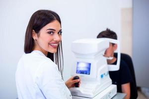 oculista femenina que usa una máquina para controlar la vista en la clínica. niño pequeño que mira el equipo y el médico prueba la pupila del ojo en la tienda óptica. concepto de cuidado ocular y salud. foto