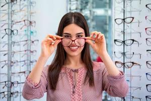 Health care, eyesight and vision concept - happy woman choosing glasses at optics store photo