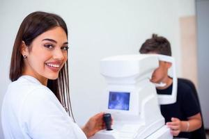 Female oculist using machine for checking eye sight in clinic. Little boy looking at equipment and doctor testing eye pupil in optical store. Concept of eye care and health. photo