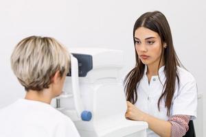 Woman visiting ophthalmologist. Pleasant short haired woman with blue eyes having her eyes checked in binocular apparatus the oculist in eyes clinic doing cornea and retina exam diagnostic photo