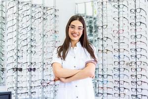 óptico vendiendo anteojos en la óptica. óptico feliz vendiendo gafas y mirando a la cámara sonriendo. Amable oftalmólogo vendiendo anteojos en la tienda de un óptico y mirando a la cámara sonriendo foto