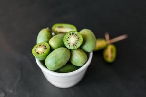 New Zealand exotic food. Berry nergi, or small kiwi. In a white plate. Grey stone background. Baby kiwi or mini kiwi fruits on stone background. Closeup view photo