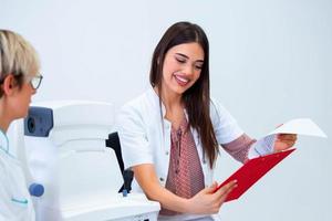 female ophthalmologist showing patient's data to a clipboard, working in an optical store. Healthcare and medicine concept photo