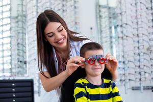 Attractive ophthalmologist examining youg boy with optometrist trial frame. Kid patient to check vision in ophthalmological clinic photo