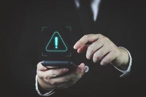 Businessman using smartphone with warning triangle showing a system error. Concepts of system maintenance, security, anti-virus, and anti-hacking access to critical data. photo