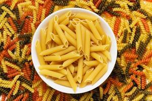 Raw pasta torti texture and penne rigate in bowl photo