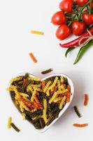 Raw pasta torti in heart bowl with cherry tomatoes and chili pepper. photo