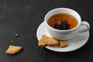 taza de té negro con galletas sobre fondo oscuro. foto