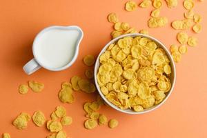 Corn flakes in white bowl and milk on orange background. photo