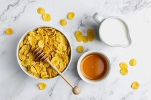 Corn flakes in white bowl with honey and milk. photo