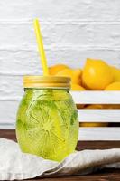 Water with mint in yellow glass, lemons in crate. photo