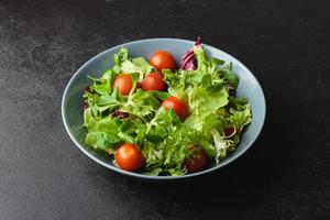 hojas de ensalada verde con tomates cherry en un tazón sobre una mesa negra. foto