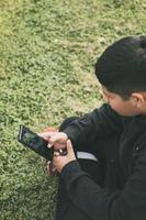 vista superior joven sentado en el parque, mirando su teléfono inteligente, enfoque selectivo foto