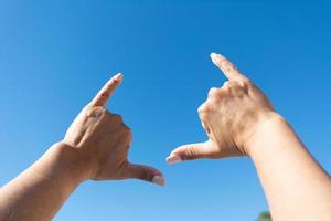 manos de mujer que muestran el signo de surfista contra el fondo del cielo azul foto