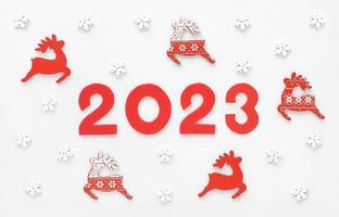 tarjeta de felicitación de año nuevo 2023 con renos rojos de santas y copos de nieve blancos. adornos de madera y fieltro años números 2 0 2 3. foto