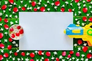 White blank paper with flowers in water bowl and water gun on banana leaf background for Songkran festival. photo