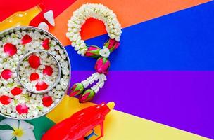 Songkran festival background with flowers in water bowls, jasmine garland, water gun, scented water and marly limestone put on colorful background. photo